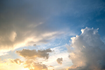 Dramatic sunset landscape with puffy clouds lit by orange setting sun and blue sky.