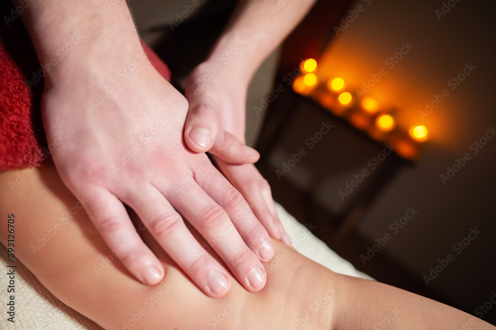 Poster close-up male hands of a masseur doing a thigh massage to a woman client in a dark room of a spa sal