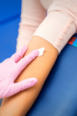 Hand of nurse applying cotton swab to arm of young woman after blood sample in the hospital