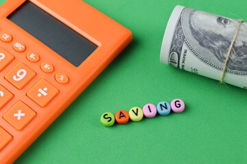 selective focus of calculator, banknote and alphabet beads written with text SAVING on a green background. Financial concept.