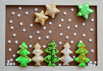 Christmas landscape composed of cookies decorated in the shape of a tree under a sky of star cookies and snowflakes on a wooden background with an external frame