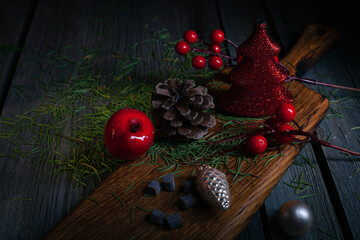 Happy New Year composition. Christmas still life made of fir needles, small red toy Christmas tree, pine cone, piece of chocolate and toys on a rustic black wooden background.