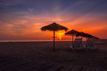 Fototapeta na wymiar Autumn sunset at the beach with straw beach hats and sun loungers