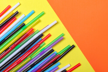 Pile of colorful cocktail straws lie on yellow and orange background.