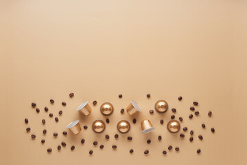 Caffeine, hot drinks and objects concept - close up of golden capsules or pods for coffee mashine with some roasted grains on beige background. Top view with space for text. Flat lay..