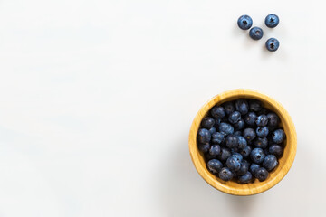 Wooden bowl of blueberries on side of white background. Purple little fresh berries in woody dish aside on table. Raw healthy blue fruit on desk with space for text.