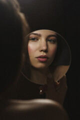 Young female holding mirror in her hand and looking at her reflection.