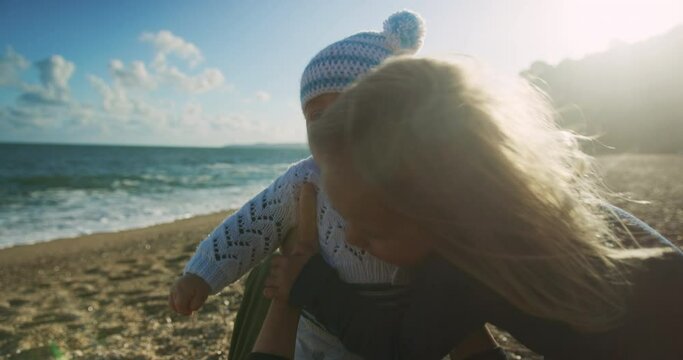A little preschooler on the beach is hugging his baby brother in the autumn sun