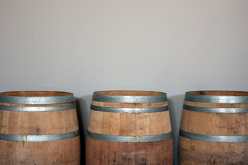 Fototapeta premium Three oak barrels stand against the wall. Wooden barrels are tied with steel hoops. Metal and natural wood of wine barrels