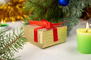 Obraz na płótnie Canvas Golden present gift box with red ribbon next to the christmas tree, candles and holiday decoration. Merry Christmas or Happy New Year greeting card. White background