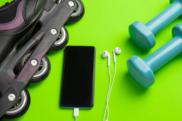 Sports equipment background.Roller skate,smartphone and headphones on green background .Top view fitness ,technology and healthy lifestyle concept.