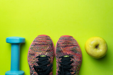 Sport fitness equipment flat lay background.Two sneakers ,apple and a dumbbell on green background with copy space text.Healthy lifestyle concept.