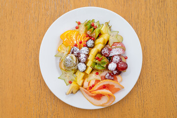 Fruit cuts of apples, pineapple, kiwi and grapes, sprinkled with icing sugar