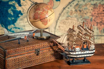 Fototapete Schiff Travel and explore the world concept. Discover the world in old style. Close up on a globe map next to a old ship model, old airplane model, luggage and binoculars. World map in background.  © Yaya Photos