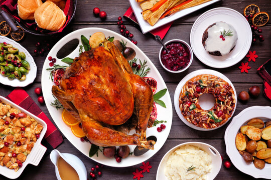 Traditional Christmas Turkey Dinner. Top View Table Scene On A Dark Wood Background. Turkey, Potatoes And Sides, Dressing, Fruit Cake And Plum Pudding.