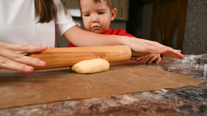 Mom shows the child how to roll the dough with a rolling pin