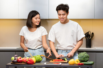 Asian Couple Cooking In Kitchen Using Tablet Preparing Dinner