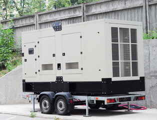 A white generator set trolley, a towable and standalone, mobile, portable industrial natural gas generator unit on four wheels standing for remote site power and emergency backup.