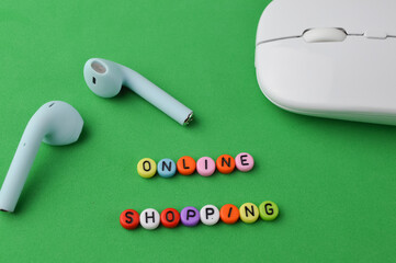 Selective focus of earphones, computer mouse and colorful alphabet beads with text ONLINE SHOPPING on a green background.
