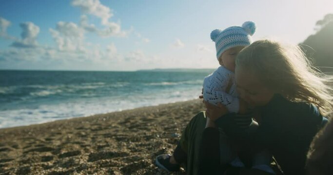 A little preschooler on the beach is hugging his baby brother in the autumn sun