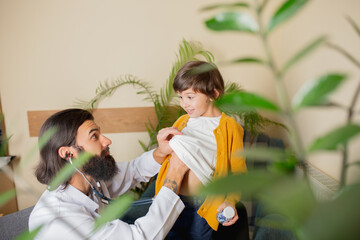 Paediatrician doctor examining a child in comfortabe medical office. Healthcare, childhood, medicine, protection and prevention concept. Little boy trust to doctor and feels calm, positive emotions.