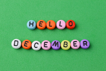 Selective focus of colorful alphabet beads with text HELLO DECEMBER on a green background.