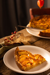 Apple pie with caramel on a wooden background, autumn bouquet in a vase, portion of pie in a plate close-up