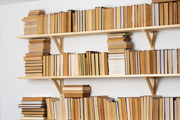 Light wooden bookshelves with hardback overturned books in white interior, home library
