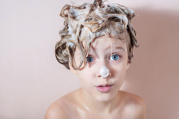 a little blonde girl washes her hair in the shower with foam on her hair and nose. playing in the bathroom with foam