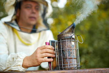 caucasian man beekeeper working in apiary, using bee smoker, nature, farming, agriculture concept. close-up photo