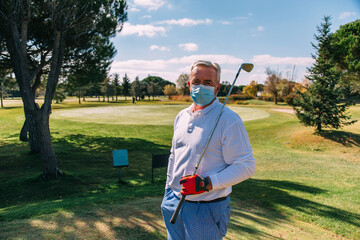 Senior golfer with disposable face mask holding golf club on golf course