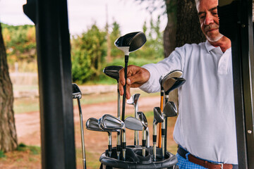Portrait of senior golfer reaching for a golf club in a bag