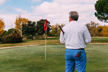 Senior golfer standing on the green looking at the flag thoughtfully