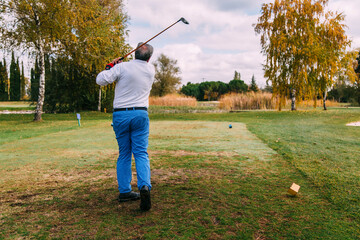Senior golfer hitting ball on a golf course in autumn