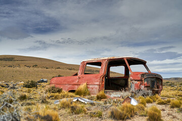 old red car wreck standing in the middle of nowhere in Patagonia in a vast landscape 