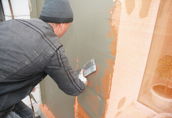 A handyman is skim coating, plastering, finishing, rendering the exterior wall, and applying cement...