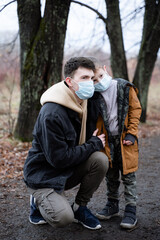 father and son look into the distance in medical masks, against the background of dry trees, pandemic time, for security reasons, sad dad and son, modern society, father and son portrait