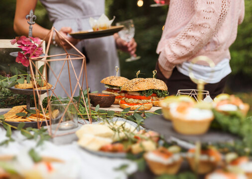 Anonymous female guests holding plates and drinksat informal garden party. Natural. lifestyle image.