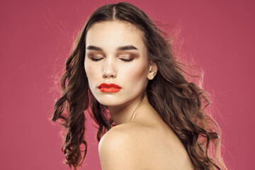 Fototapeta premium Beautiful brunette woman with makeup on her face on a pink background naked shoulders