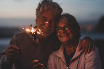 new year. close up of seniors celebrating the new year together at the beach with sparklers lights