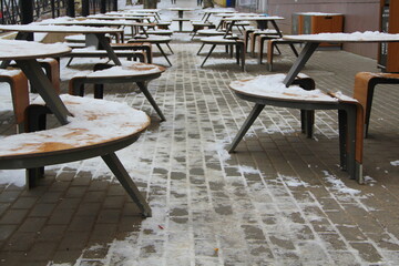 Tables and benches covered with snow stand on the city street on a pavement next to the restaurant winter in Russia