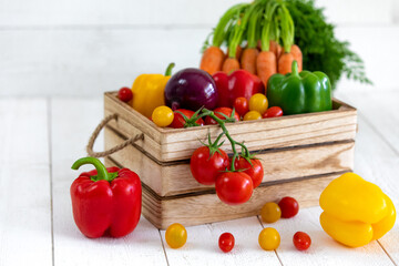 Une caisse de légumes fraiche avec des tomates, des oignons,des poivrons,des carottes,des tomates cerises avec de belles couleurs éclatantes rouges, jaunes,vert et oranges sur un fond de bardage blanc