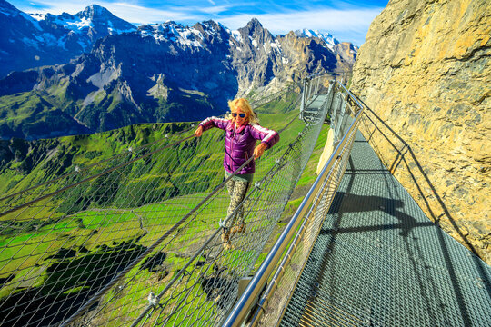 Thrill walk on Schilthorn, Bernese Prealps, Canton of Bern in Switzerland. Caucasian tourist woman walks on a net between high rock faces at mid-station Birg, 2677, above village of Murren.