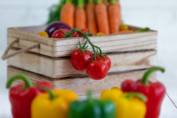 Une caisse de légumes fraiche avec des tomates, des oignons,des poivrons,des carottes,des tomates cerises avec de belles couleurs éclatantes rouges, jaunes,vert et oranges sur un fond de bardage blanc