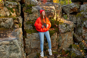Fototapeta premium beautiful female with long red hair loves travelling on mountains, stand surrounded by big rocks and stones alone, use binoculars for better contemplation of nature
