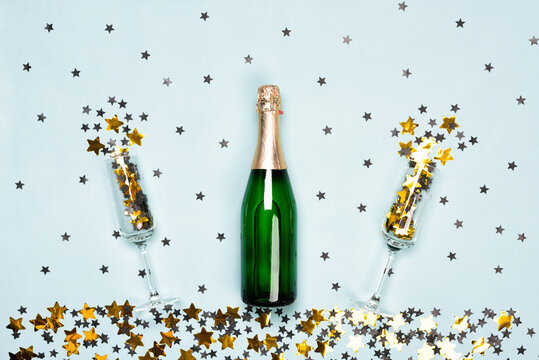 Champagne bottle with black and gold stars and circle confetti on the blue background with black and gold stars and circle confetti. Christmas or New Year festive concept. Top view and flat lay.