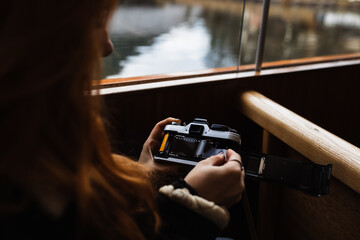 Side view of crop unrecognizable female traveler inserting film roll into old fashioned photo camera during boat trip on lake in autumn day