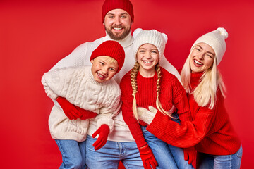 portrait of family having fun in winter clothes isolated over red studio background, young parents and children enjoy winter time, christmas