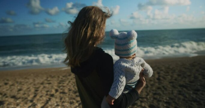 A young mother is walking on the beach with her baby in a sling