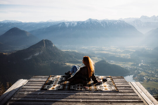 Back view of unrecognizable female tourist sitting at viewpoint in mountains and observing amazing scenery in morning
